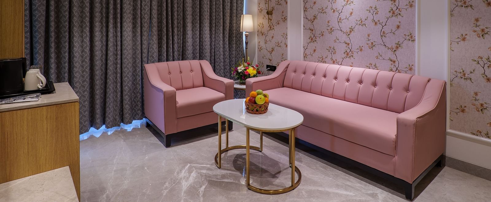 A seating area including a pink sofa, armchairs, a round table, and patterned wallpaper under warm lighting - Melior Inn