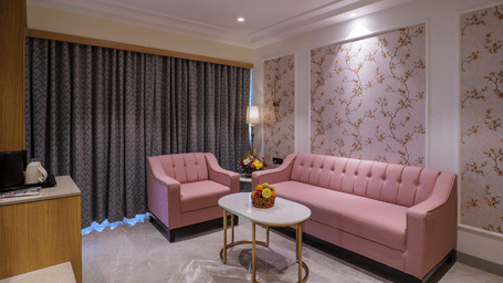 A seating area including a pink sofa, armchairs, a round table, and patterned wallpaper under warm lighting - Melior Inn