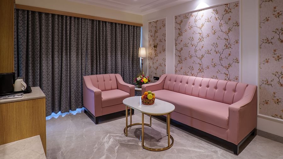 A seating area including a pink sofa, armchairs, a round table, and patterned wallpaper under warm lighting - Melior Inn