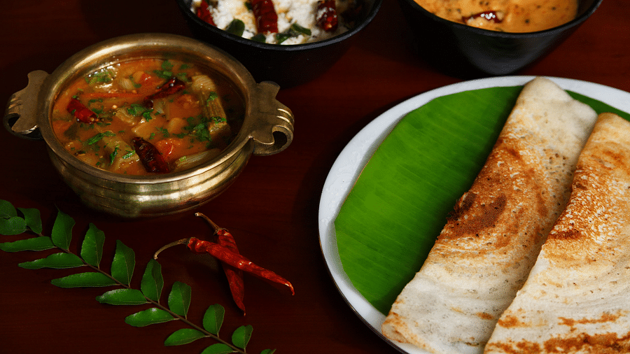 A top-down view of a plate with South Indian cuisine, what appears to be dosa, sambar, and chutneys.