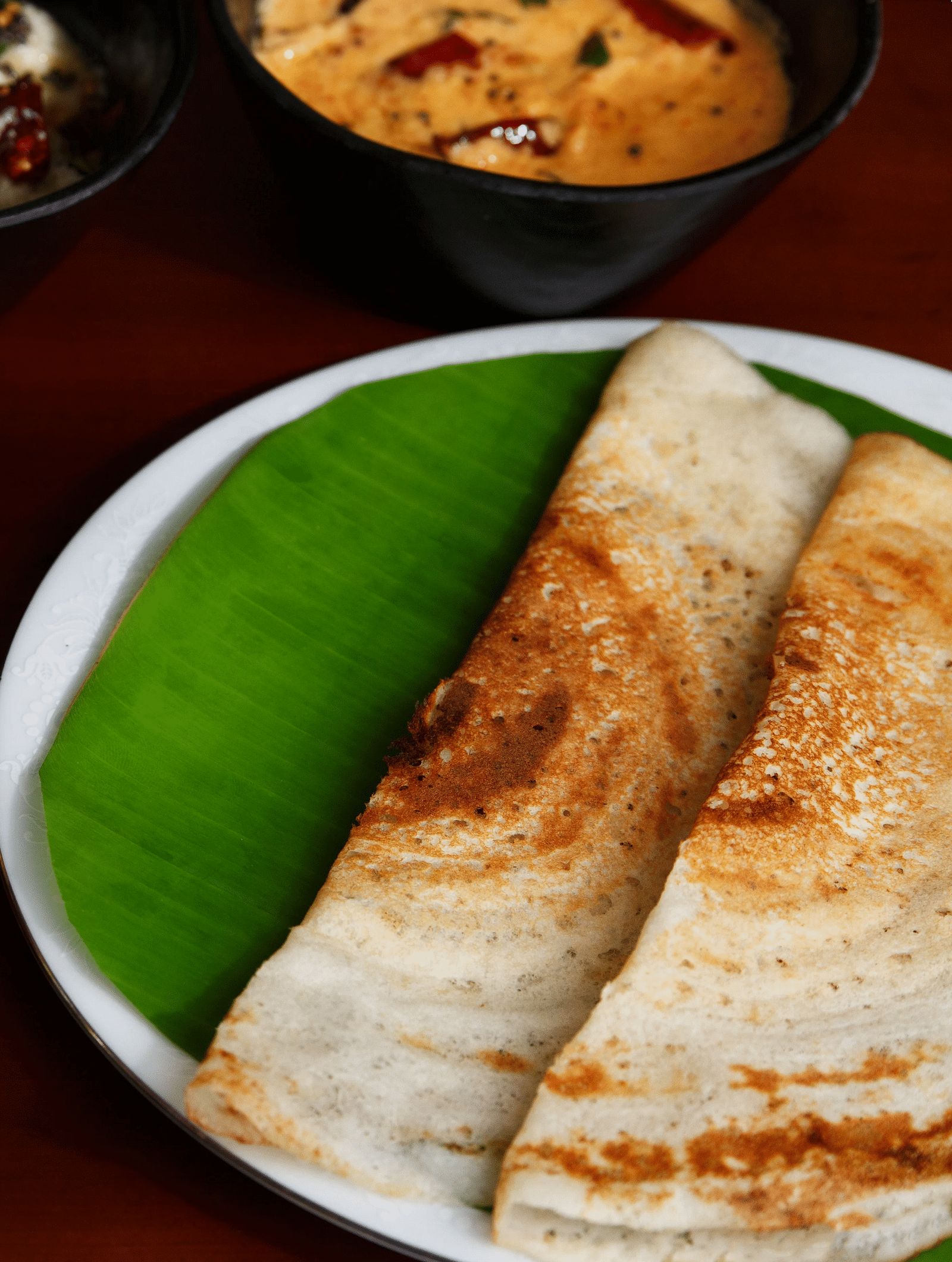 A top-down view of a plate with South Indian cuisine, what appears to be dosa, sambar, and chutneys.