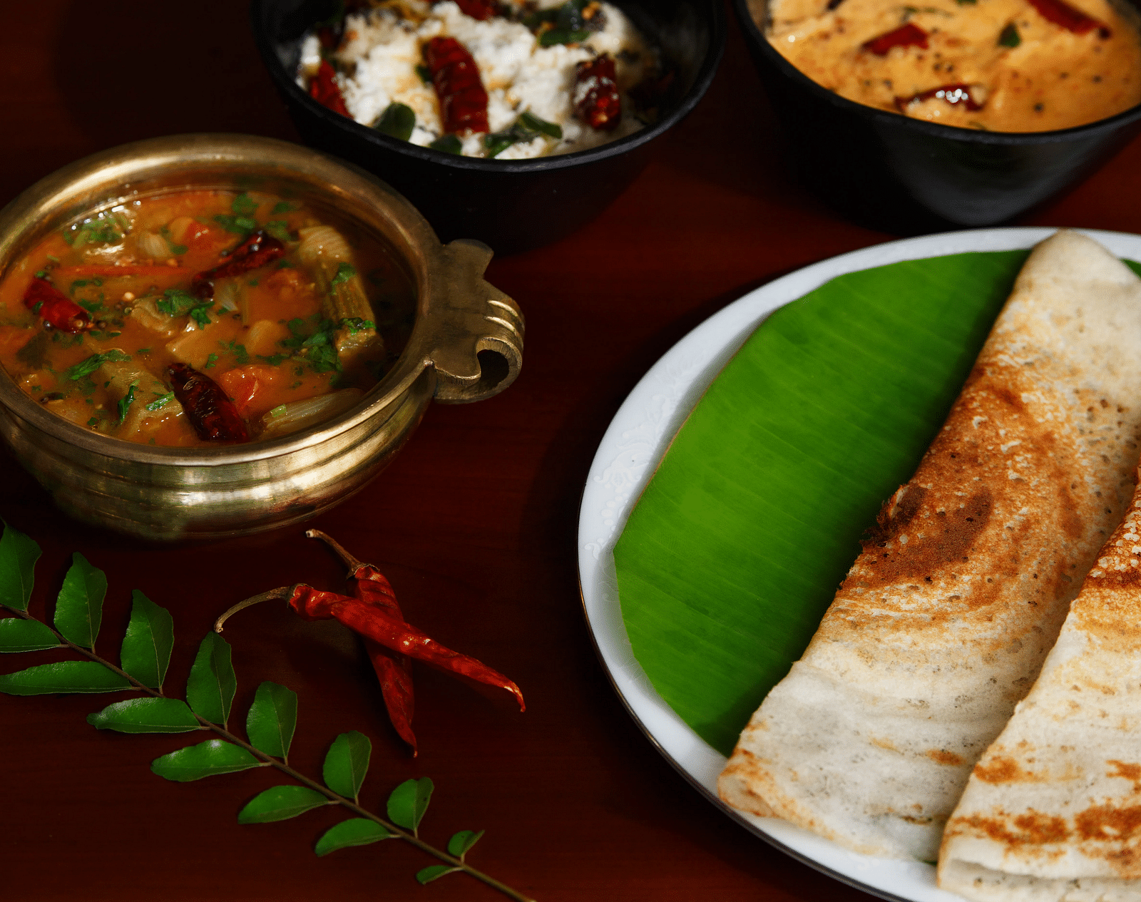 A top-down view of a plate with South Indian cuisine, what appears to be dosa, sambar, and chutneys.