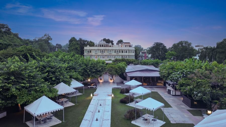 Exterior view of the back of Ram Pratap Palace in Udaipur, with a large garden, outdoor dining tents, and a central walkway at dusk.