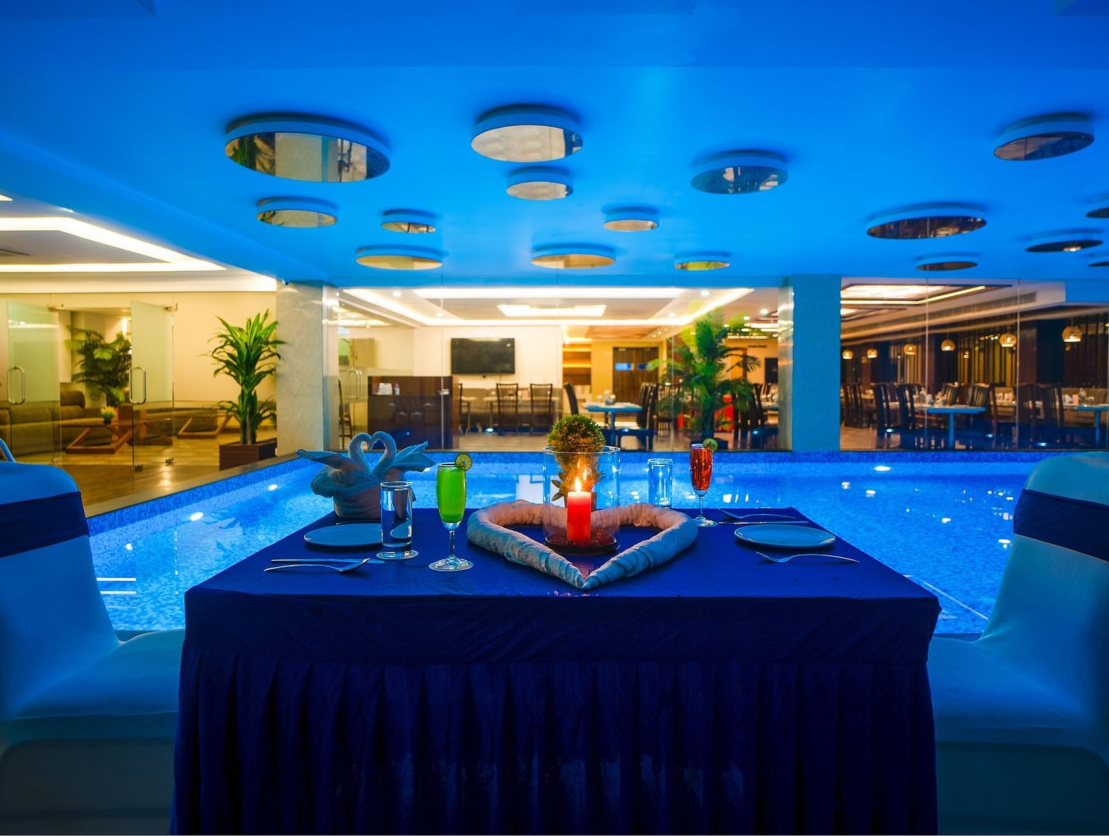Poolside dining setup with a table and chairs under ceiling lights at Mansha Regency, Port Blair.