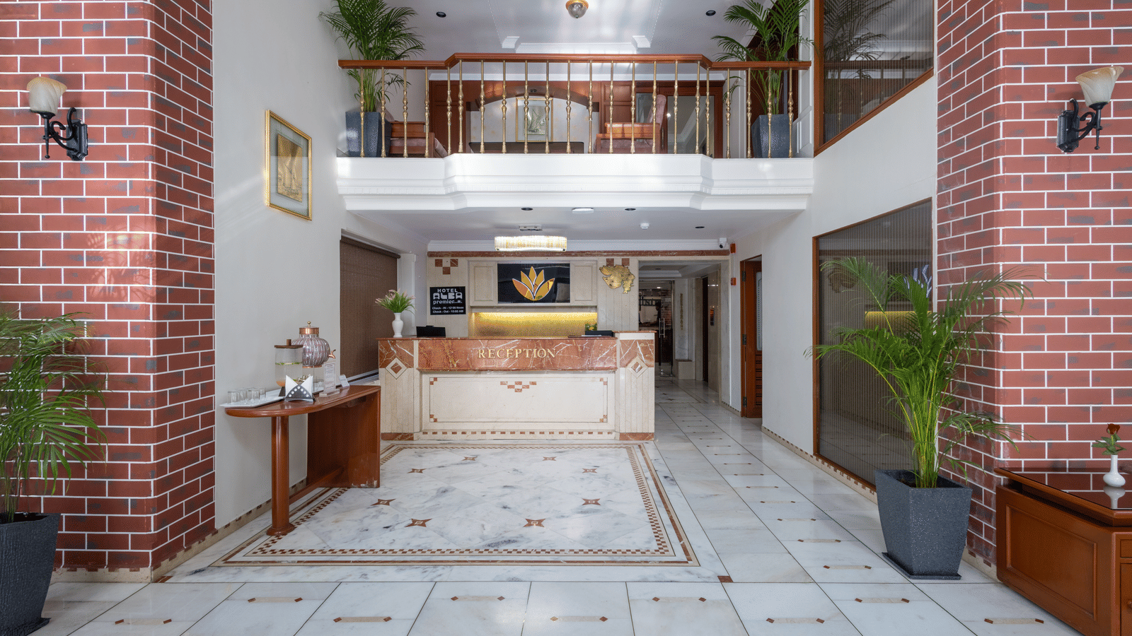 Two-storey hotel reception lobby with marble flooring, exposed red brick walls, and a wooden check-in counter at Pravasa Stay, Vadodara.