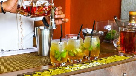 A bar counter displaying various alcoholic drinks and a man pouring liquid into a mixing glass.