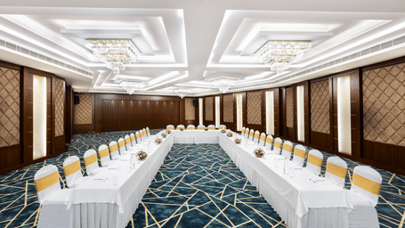 A hall at Jenneys Residency with chairs, chandeliers, and checkered floor.