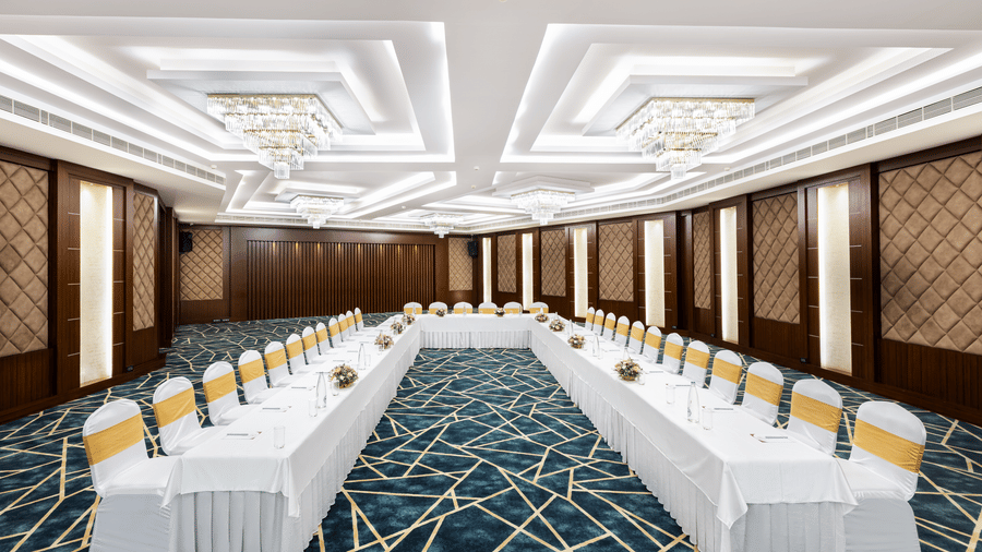 A hall at Jenneys Residency with chairs, chandeliers, and checkered floor.