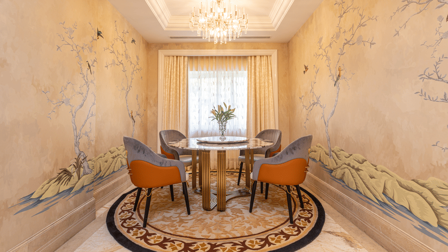 image of an elegant dining area with a round table in the middle with cushioned chairs surrounding it at our Lutyens luxury suite - The Claridges New Delhi