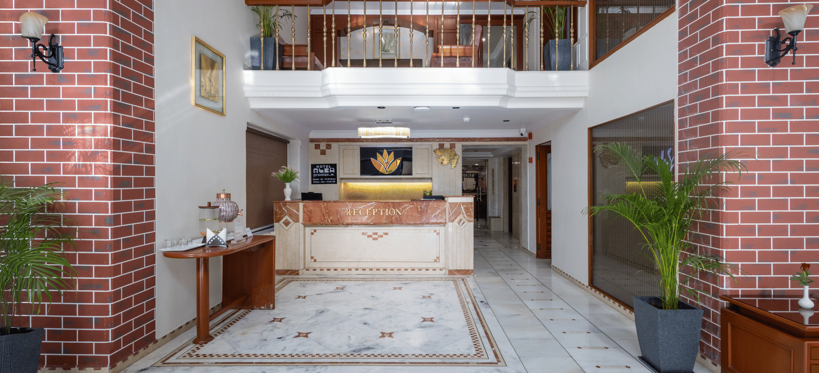 Two-storey hotel reception lobby with marble flooring, exposed red brick walls, and a wooden check-in counter at Pravasa Stay, Vadodara.