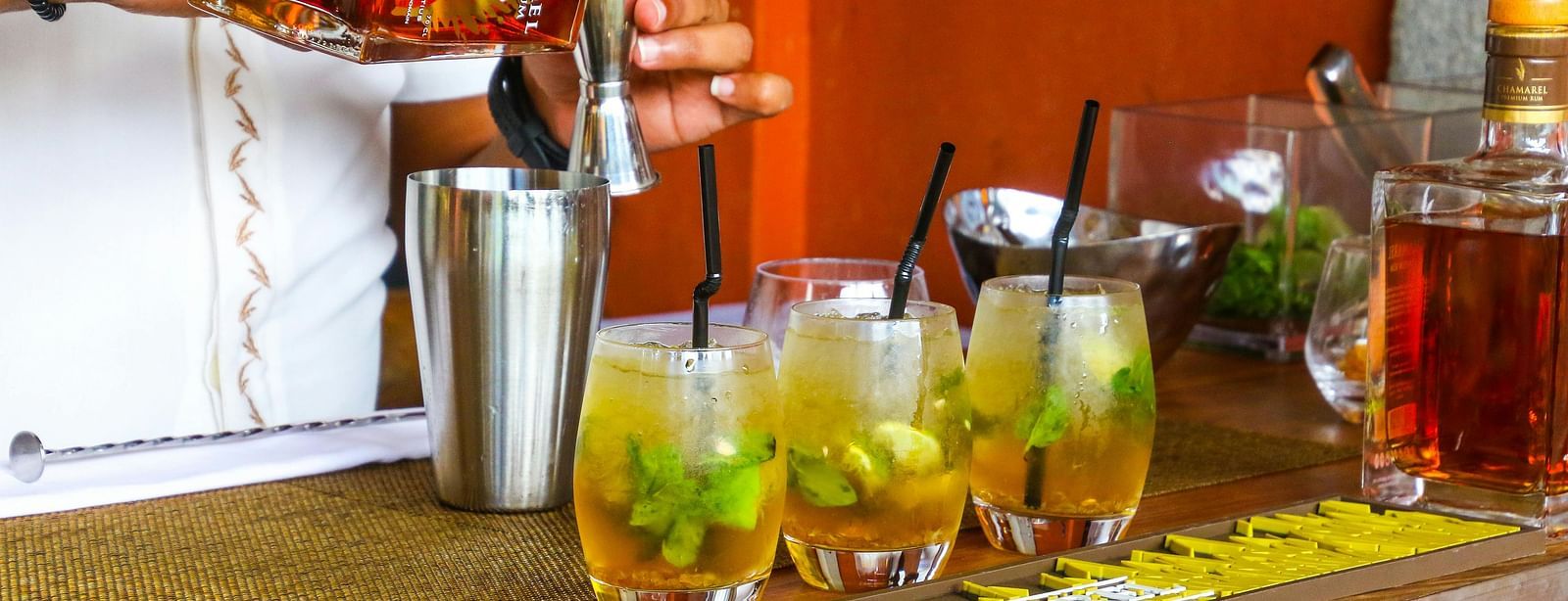 A bar counter displaying various alcoholic drinks and a man pouring liquid into a mixing glass.