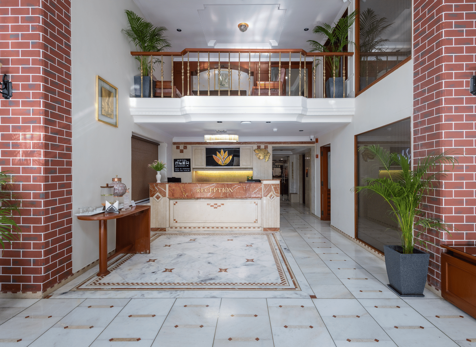 Two-storey hotel reception lobby with marble flooring, exposed red brick walls, and a wooden check-in counter at Pravasa Stay, Vadodara.