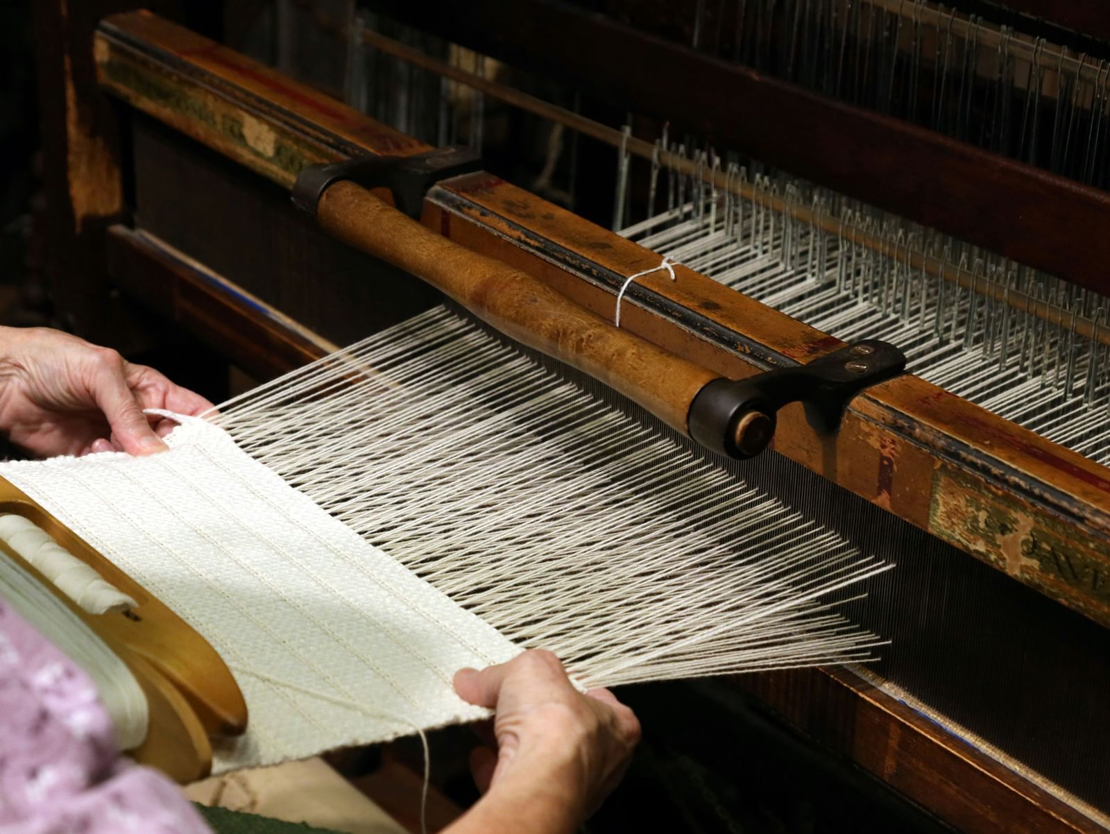 Close-up of a person weaving fabric on a traditional handloom machine.