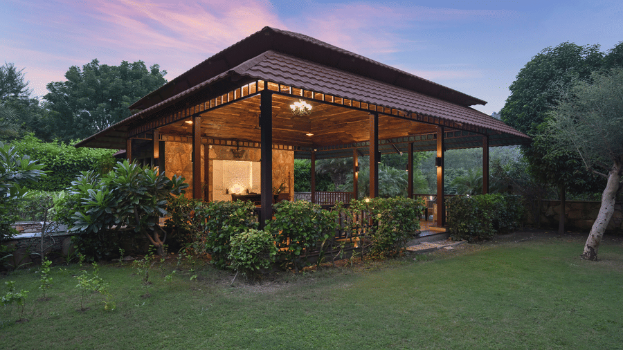 A modern open-walled building with a tiered roof situated in a garden at twilight | Anandam Jungle Retreat Resort, Udaipur