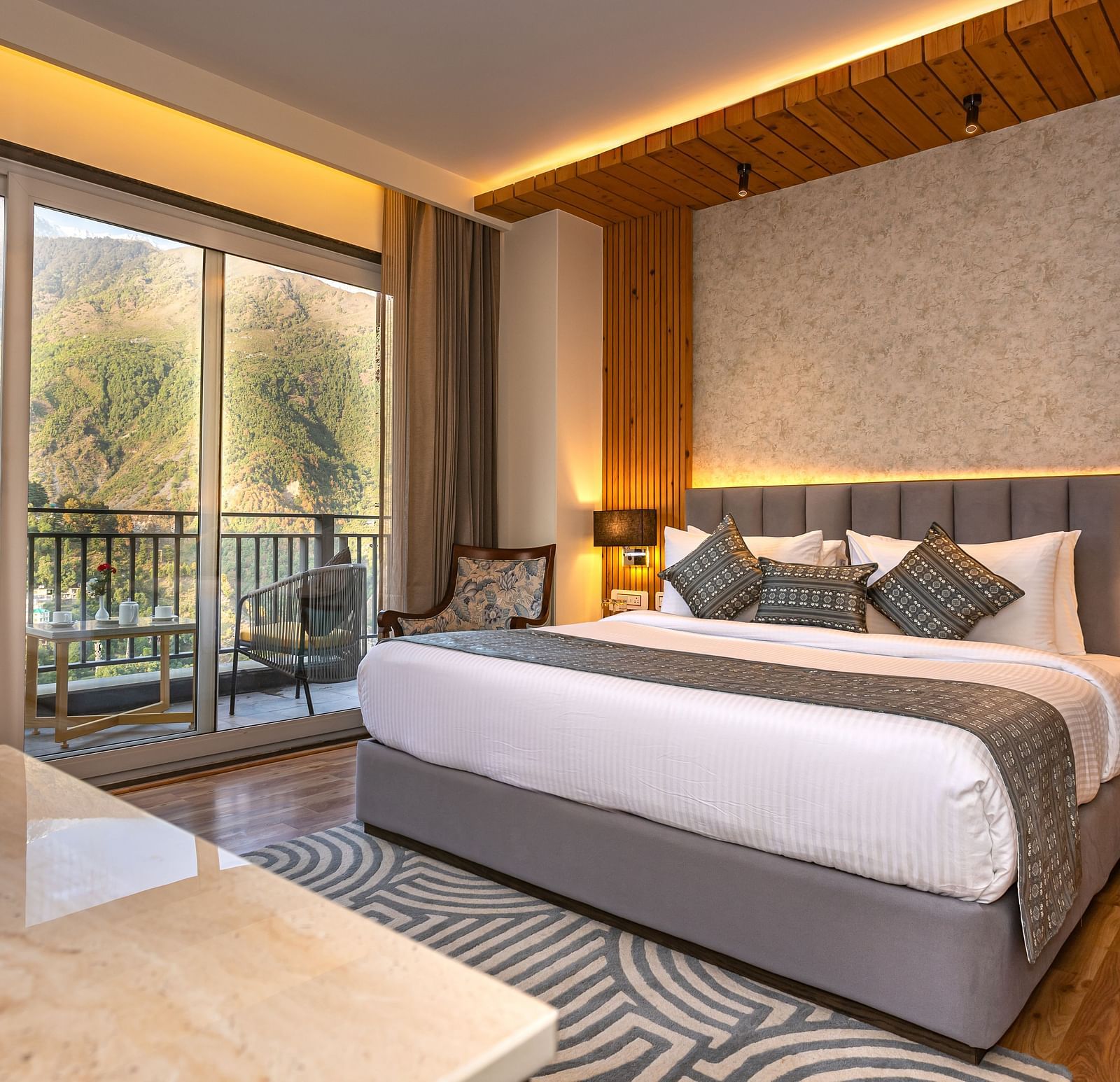 An image of a Suite with a bed, bed side table, lamp shades, and an expansive glass door leading to the balcony - The Belvedere Himalayan Retreat, McLeodganj