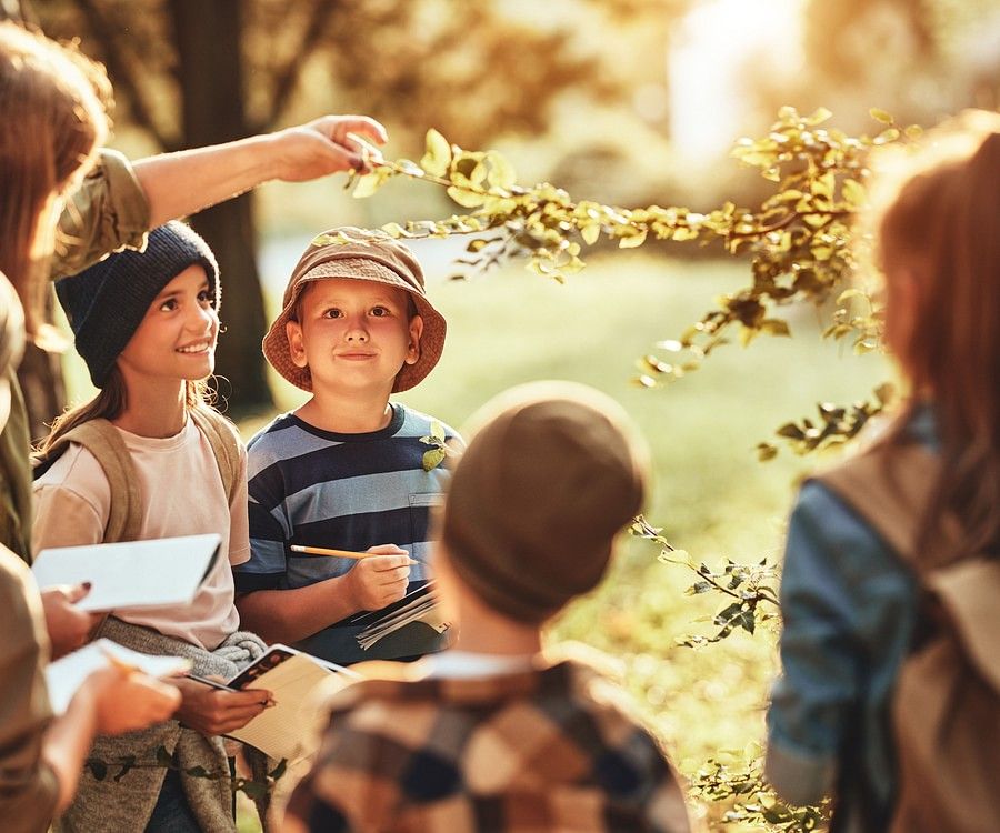 alt-text a group of children taking notes at a park with their teacher during daytime