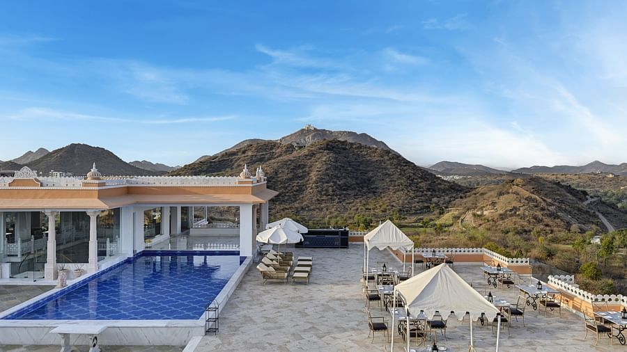 Shot of Khas Mahal by Fateh Collection, Udaipur with a swimming pool set against a backdrop of mountains and a clear blue sky.