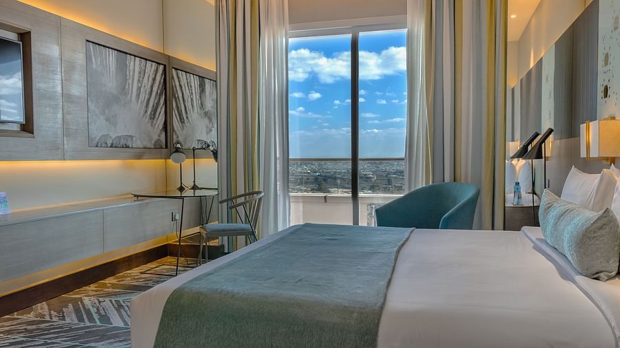 A cozy bedroom with a large bed and a scenic window view at Neelkanth Sarovar Premiere Lusaka