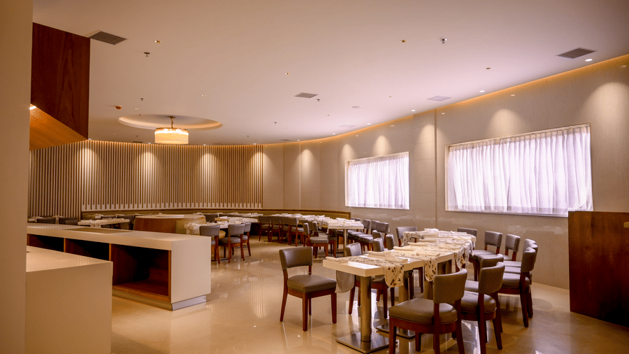 An indoor restaurant dining area arranged with various tables, upholstered chairs, and a long serving counter at Tiara by MPS.