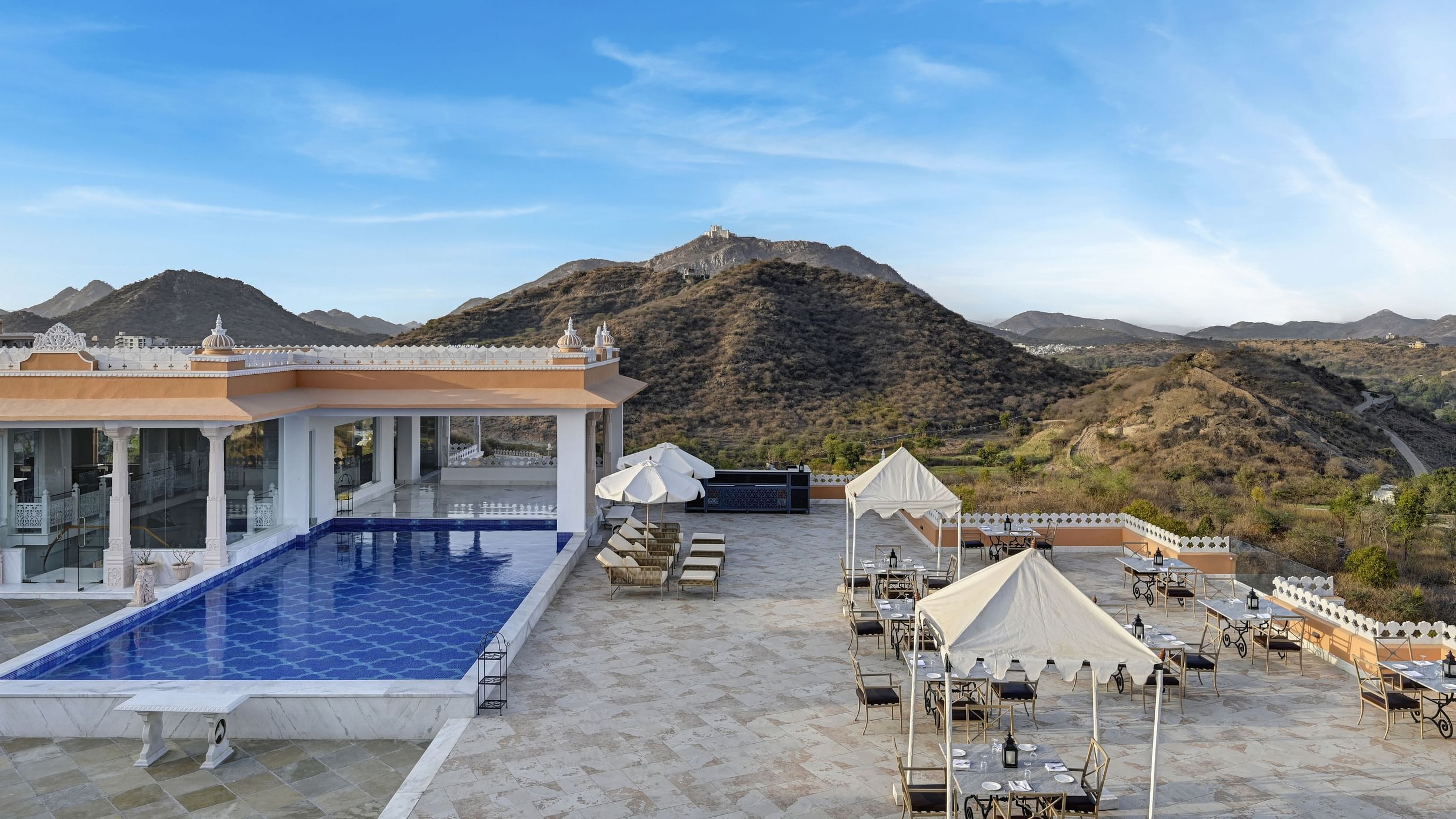 Shot of Khas Mahal by Fateh Collection, Udaipur with a swimming pool set against a backdrop of mountains and a clear blue sky.