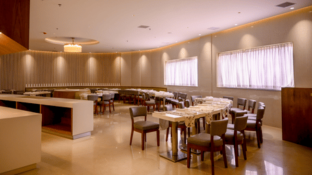 An indoor restaurant dining area arranged with various tables, upholstered chairs, and a long serving counter at Tiara by MPS.