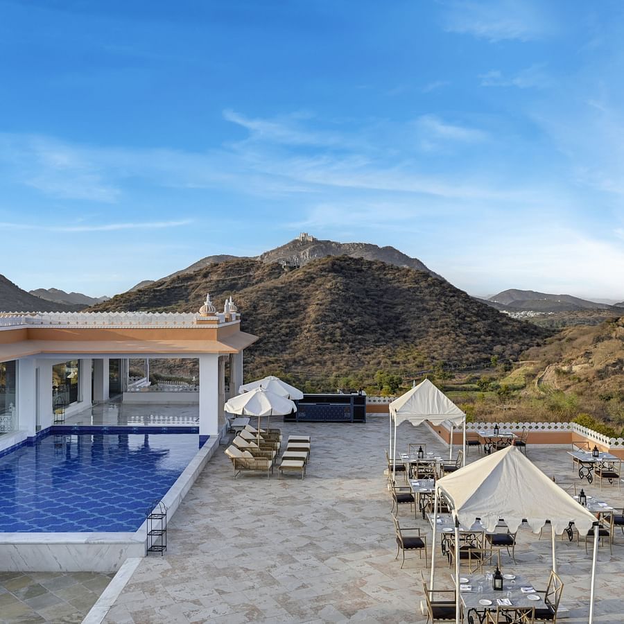 Shot of Fatehgarh Khas Mahal Wing, Udaipur with a swimming pool set against a backdrop of mountains and a clear blue sky.