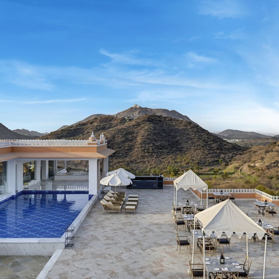 Shot of Fatehgarh Khas Mahal Wing, Udaipur with a swimming pool set against a backdrop of mountains and a clear blue sky.