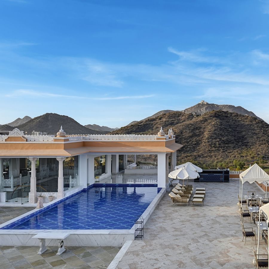 Shot of Khas Mahal by Fateh Collection, Udaipur with a swimming pool set against a backdrop of mountains and a clear blue sky.
