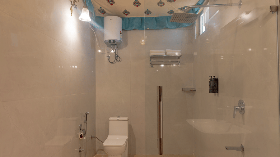 A bathroom at Estherea Bagh, Ranthambore, featuring tiled walls, a modern toilet, a glass shower partition, and a patterned ceiling fabric.