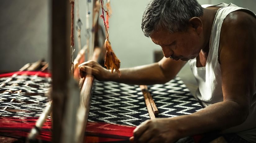 Elderly artisan focused on weaving a traditional patterned fabric on a handloom.