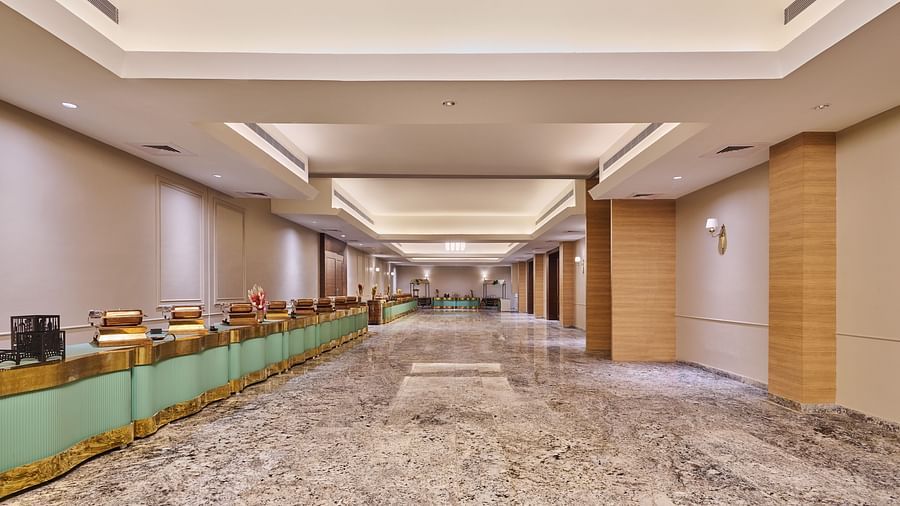 Spacious hotel lobby with a long marble floor, modern lighting, a reception desk with green and gold accents on the left, and a clean, minimalist design with light-coloured walls and wooden columns - Voyage The Solitaire Bliss.