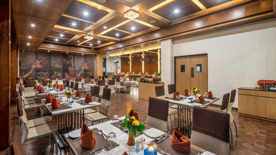 A spacious and elegantly designed restaurant with well-set tables adorned with flowers and buffet stations at Lords Inn Somnath.