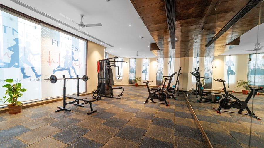 Fitness centre at Inde Reva Resorts Rishhikesh with treadmills, weights, and floor-to-ceiling mirrors on slate tile flooring.