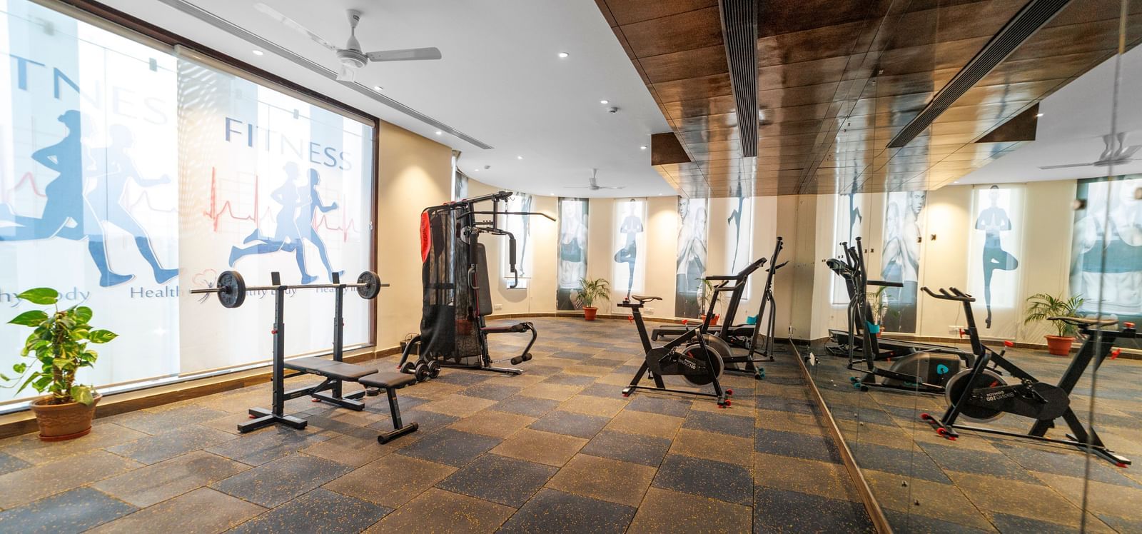 Fitness centre at Inde Reva Resorts Rishhikesh with treadmills, weights, and floor-to-ceiling mirrors on slate tile flooring.