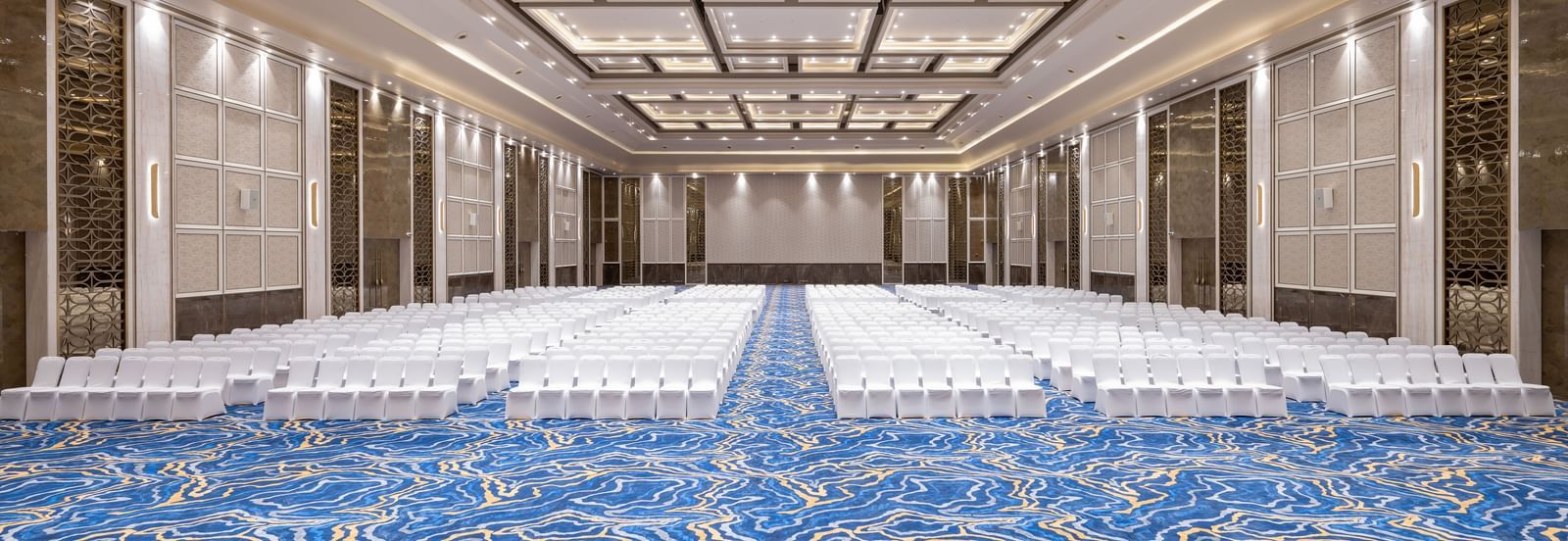 A grand ballroom with theatre seating and decorative ceiling panels at Merlis Hotel, Coimbatore - One of the best Wedding Venues in Coimbatore.