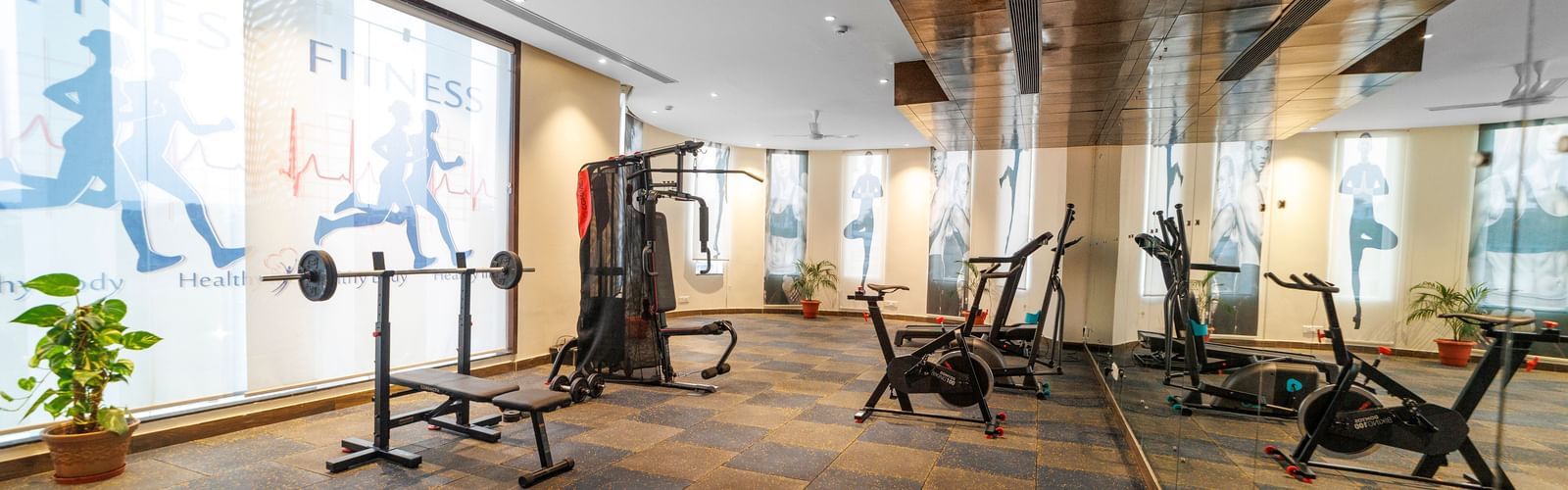 Fitness centre at Inde Reva Resorts Rishhikesh with treadmills, weights, and floor-to-ceiling mirrors on slate tile flooring.
