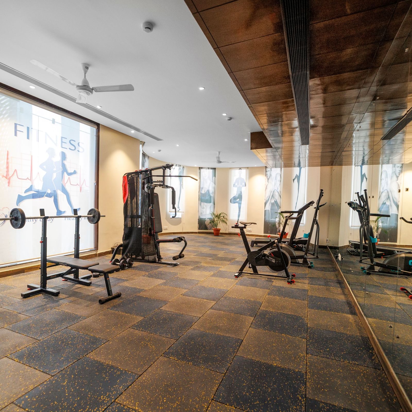 Fitness centre at Inde Reva Resorts Rishhikesh with treadmills, weights, and floor-to-ceiling mirrors on slate tile flooring.