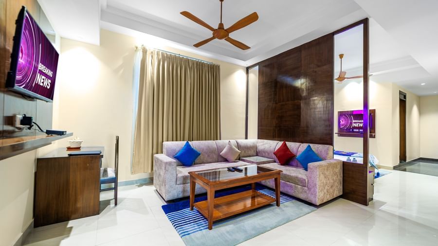 Room at Inde Reva Resorts Rishhikesh with seating area,TV, coffee table, ceiling fan, and full-length curtains.
