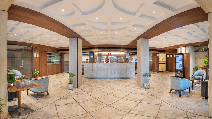 reception at Lords Eco Inn desk flanked by large columns, a light-tiled floor with decorative patterns, and wooden beams across the ceiling.