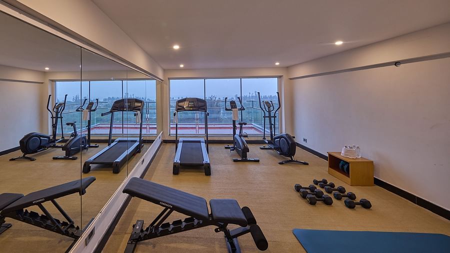 a treadmill, a stationary bike, an elliptical trainer, dumbbells, a yoga mat, and a bench in the fitness centre at Grand Continent, Mahabalipuram