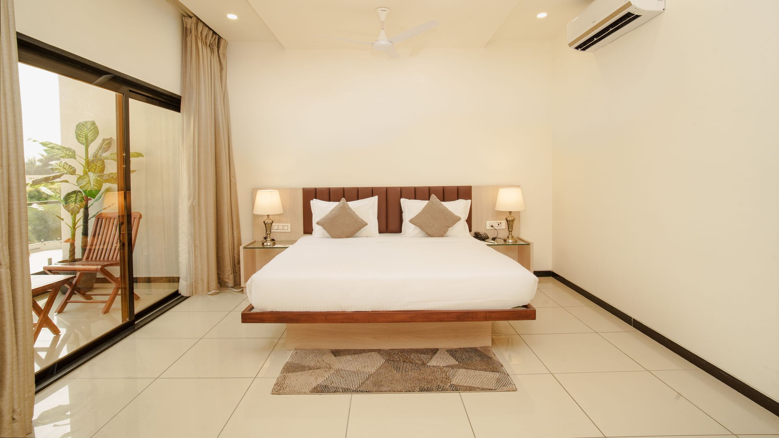 Clean hotel room featuring a large bed, minimalist wood furniture, and a sliding glass door at Arawali Ananta Elite, Jaipur.