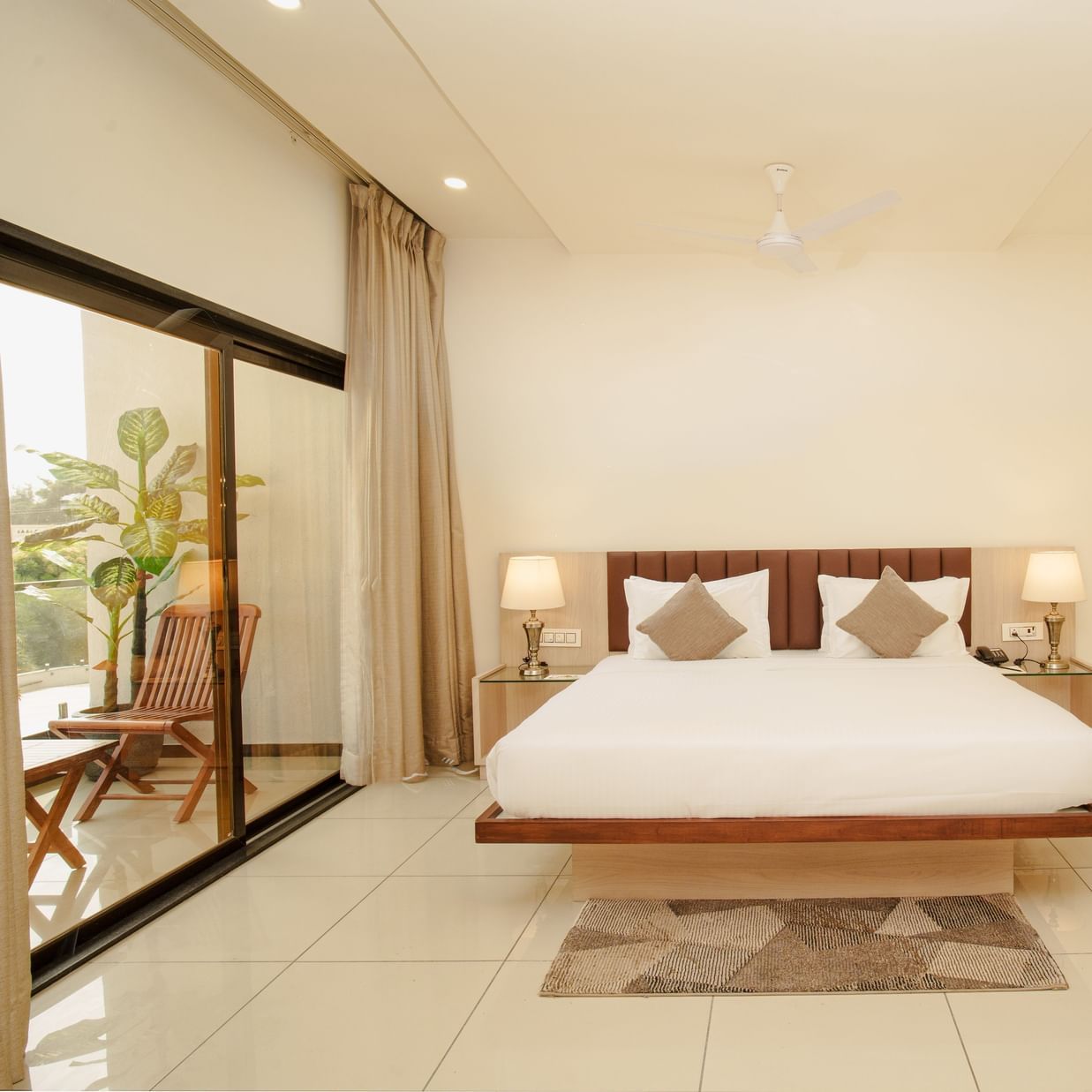 Clean hotel room featuring a large bed, minimalist wood furniture, and a sliding glass door at Arawali Ananta Elite, Jaipur.