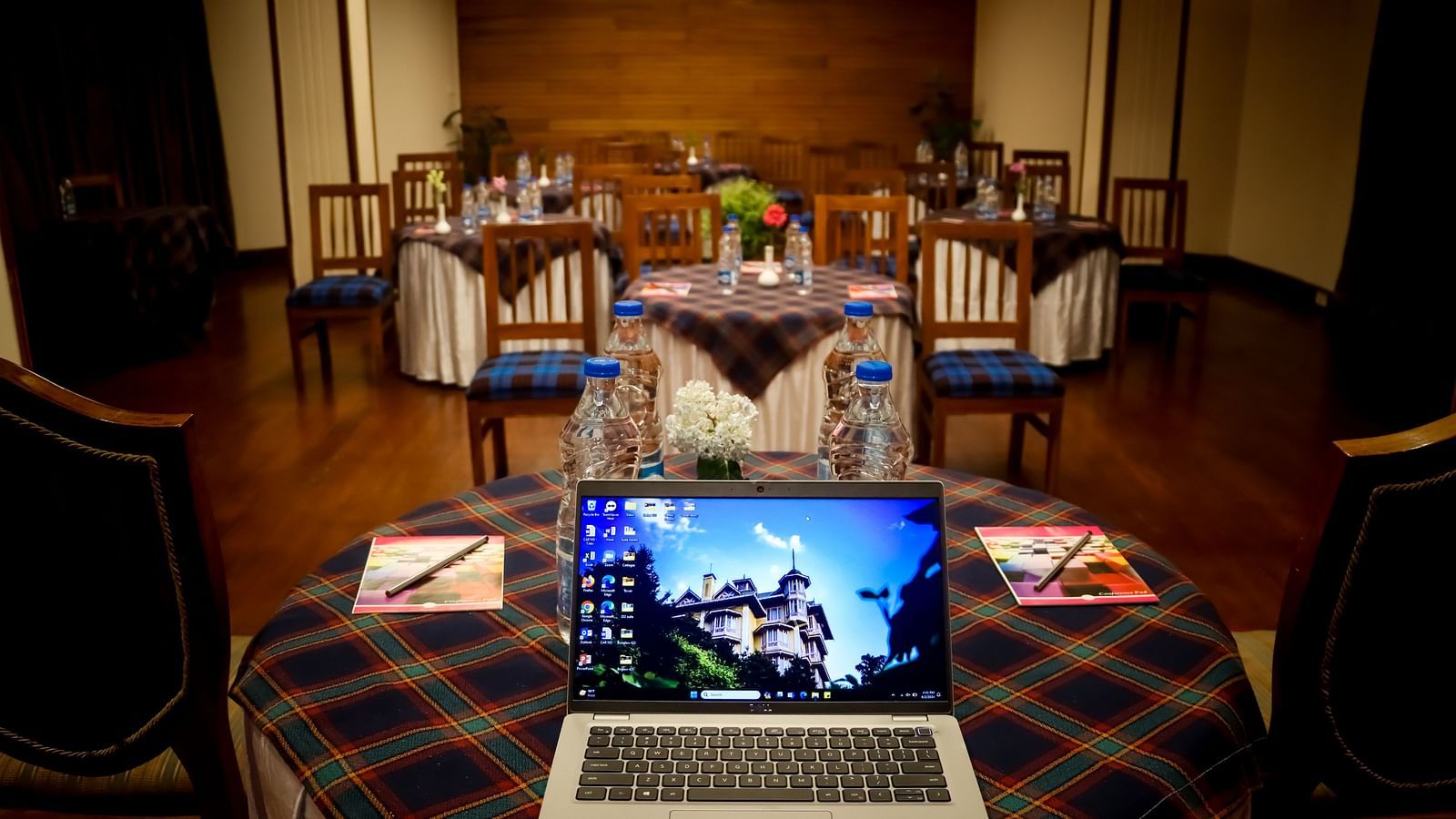 Banquet Hall at Cedar Inn, Darjeeling set for a meeting with a laptop, water bottles, notepads, and chairs arranged around tartan-covered tables.