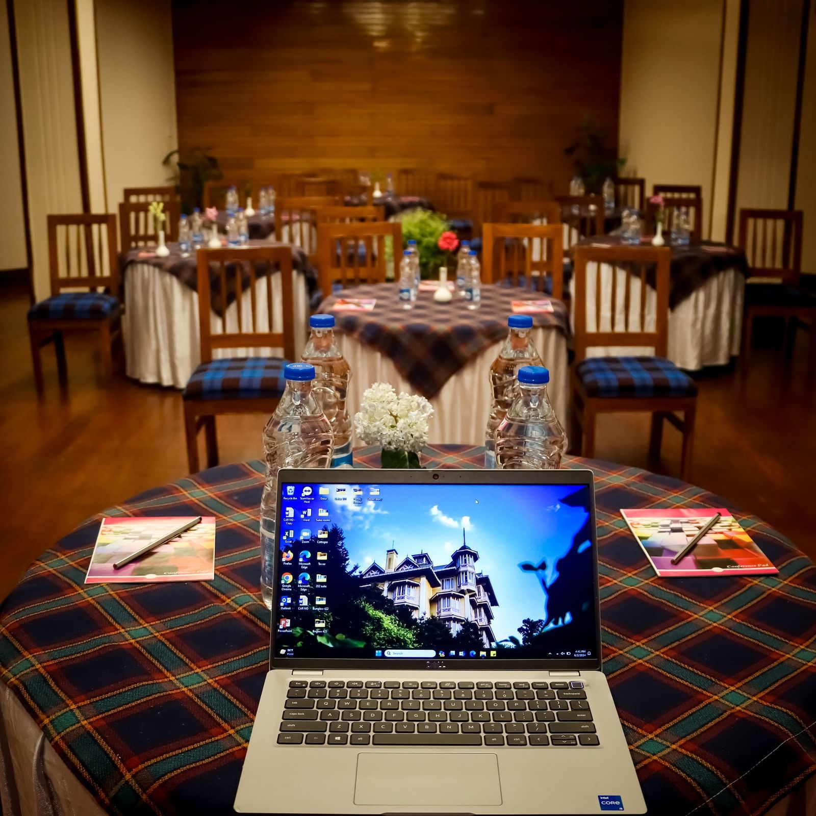 Banquet Hall at Cedar Inn, Darjeeling set for a meeting with a laptop, water bottles, notepads, and chairs arranged around tartan-covered tables.