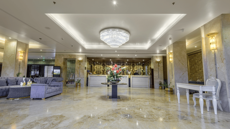 A luxurious hotel lobby featuring marble floors, a large crystal chandelier, and a purple velvet sofa lounge under warm, recessed lighting at Golden Tulip Kukas, Jaipur.