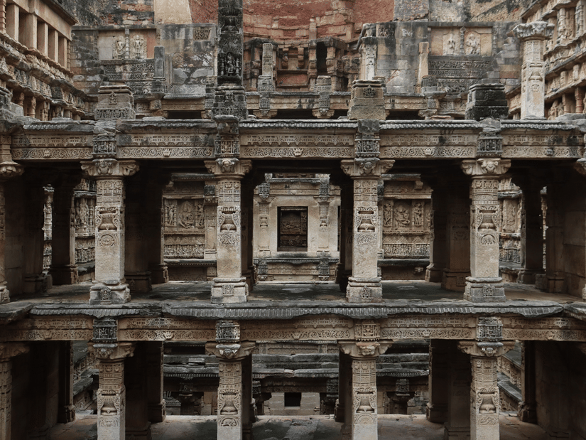 The intricate, multi-tiered stone architecture and pillars of a historic Indian stepwell are shown in detail.