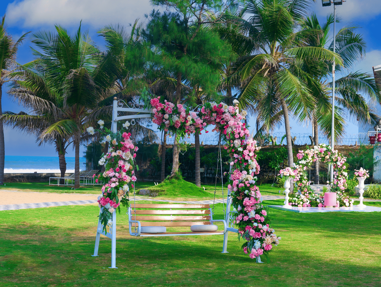 A swing decorated with pastel flowers on a green lawn in front of coconut trees - Grande Bay Resort & Spa, Mamallapuram