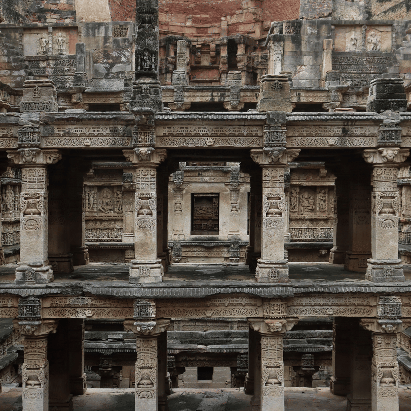 The intricate, multi-tiered stone architecture and pillars of a historic Indian stepwell are shown in detail.