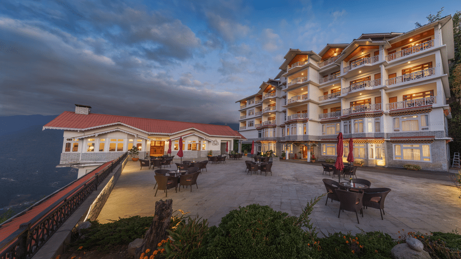 The facade of Summit Norbu Ghang - The Signature Collection, Gangtok, with balconies, windows, and outdoor seating area at dusk.