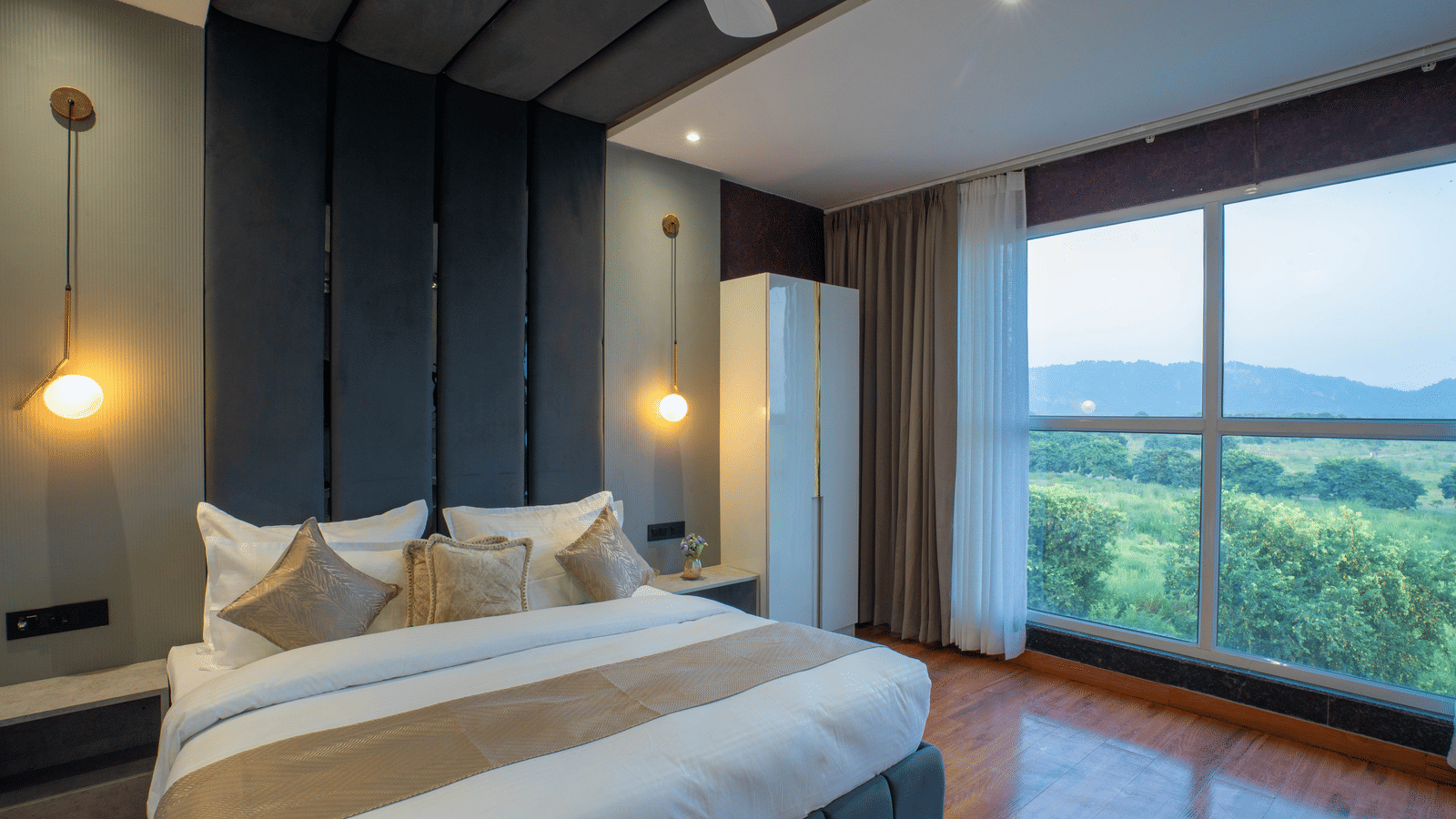 A guest room at Sukoon by the Ganges featuring a dark panelled headboard and a large window with beautiful green scenery.